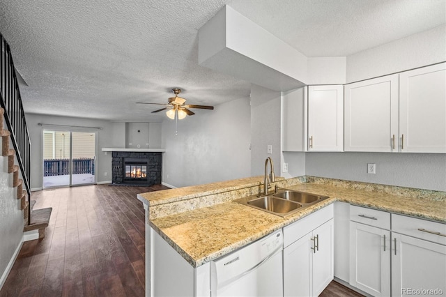 kitchen featuring a stone fireplace, sink, dishwasher, kitchen peninsula, and white cabinets