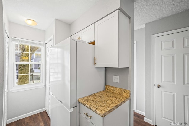 kitchen featuring white cabinetry, dark hardwood / wood-style flooring, white refrigerator, light stone countertops, and a textured ceiling