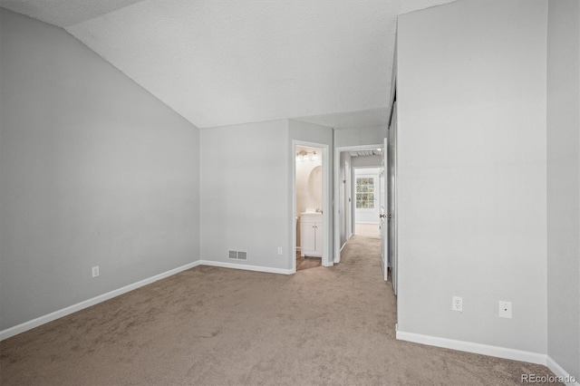 carpeted spare room with vaulted ceiling and a textured ceiling