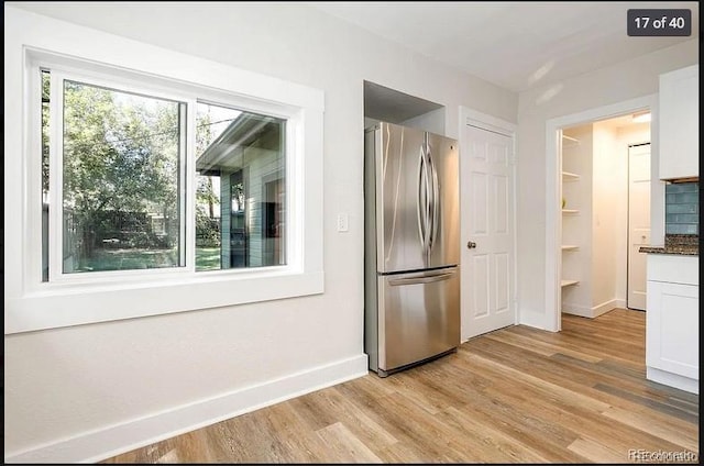 kitchen featuring dark stone countertops, stainless steel fridge, white cabinets, and light hardwood / wood-style floors