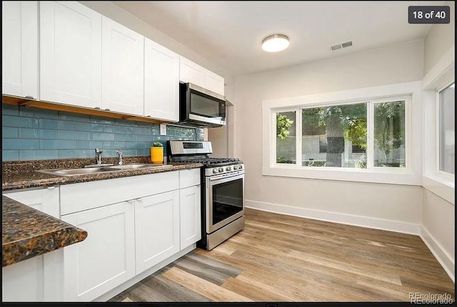 kitchen with decorative backsplash, appliances with stainless steel finishes, sink, light hardwood / wood-style floors, and white cabinetry