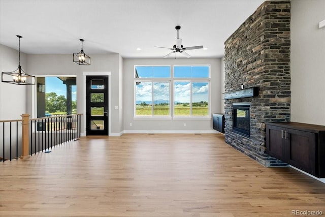 unfurnished living room featuring ceiling fan with notable chandelier, a stone fireplace, and light hardwood / wood-style flooring