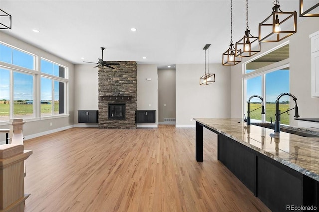 kitchen with a fireplace, light wood-type flooring, light stone counters, ceiling fan with notable chandelier, and pendant lighting