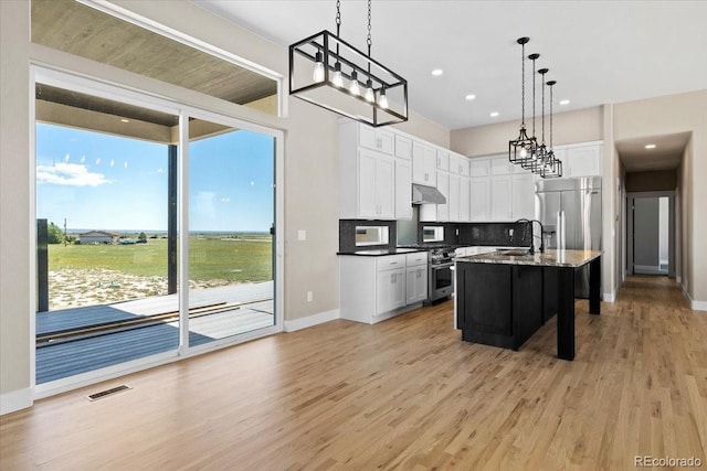 kitchen featuring light hardwood / wood-style flooring, backsplash, hanging light fixtures, a kitchen island with sink, and high end appliances