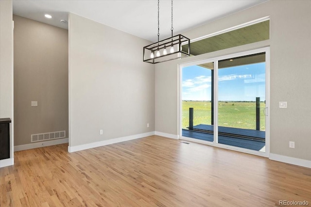 empty room featuring a notable chandelier and light hardwood / wood-style flooring