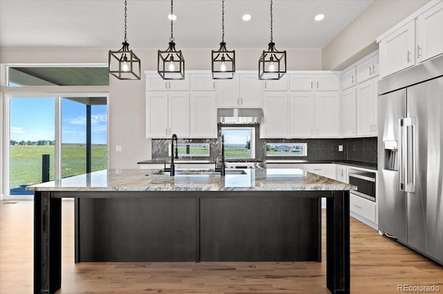 kitchen with backsplash, dark stone countertops, light wood-type flooring, a kitchen island with sink, and built in appliances