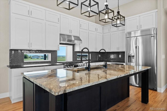 kitchen featuring backsplash, light hardwood / wood-style flooring, wall chimney exhaust hood, built in refrigerator, and a center island with sink