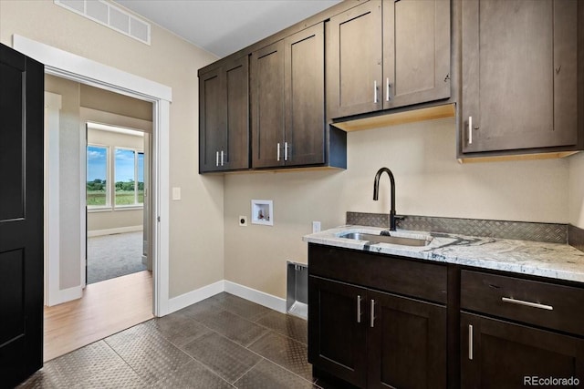 kitchen with sink, dark tile patterned floors, dark brown cabinets, and light stone countertops