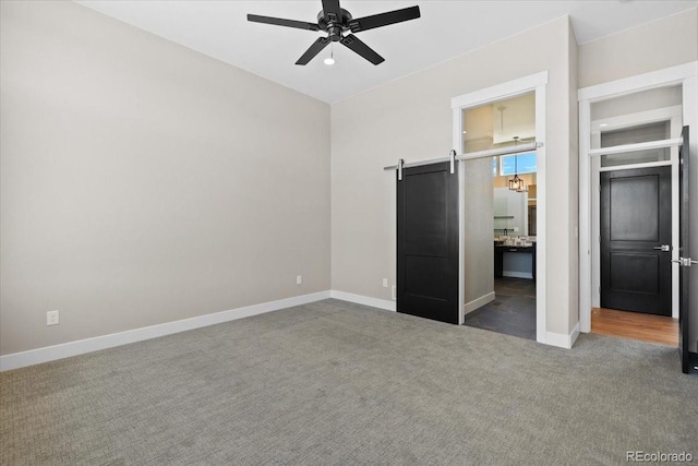 unfurnished bedroom with ceiling fan, a barn door, and dark carpet