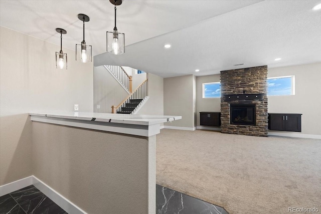 interior space featuring dark colored carpet, a wealth of natural light, a stone fireplace, and pendant lighting