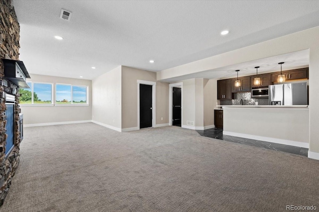 unfurnished living room featuring a stone fireplace, dark carpet, and a textured ceiling