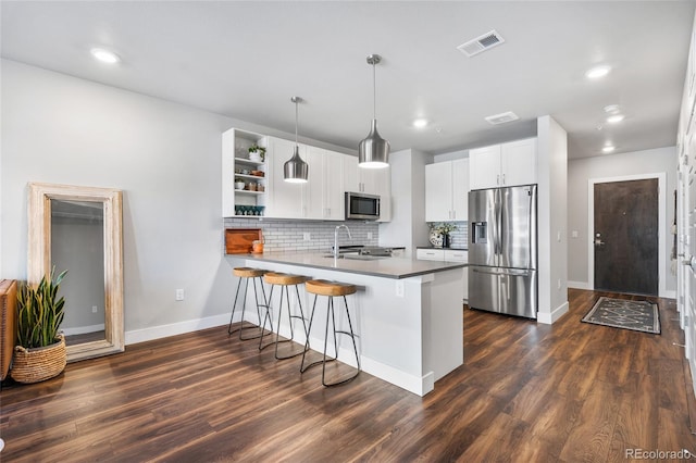 kitchen featuring appliances with stainless steel finishes, pendant lighting, white cabinetry, a breakfast bar area, and kitchen peninsula