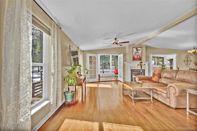 living area featuring baseboards, a glass covered fireplace, hardwood / wood-style flooring, vaulted ceiling with beams, and ceiling fan with notable chandelier