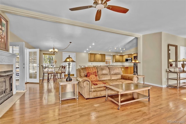 living room featuring light wood-type flooring, a fireplace, baseboards, and ceiling fan with notable chandelier