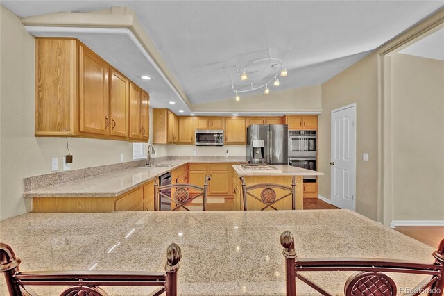 kitchen with a sink, vaulted ceiling, stainless steel appliances, track lighting, and recessed lighting