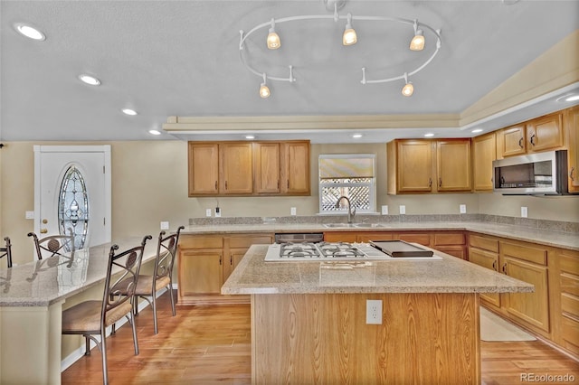 kitchen with a kitchen island, light wood-style floors, stainless steel microwave, and a sink