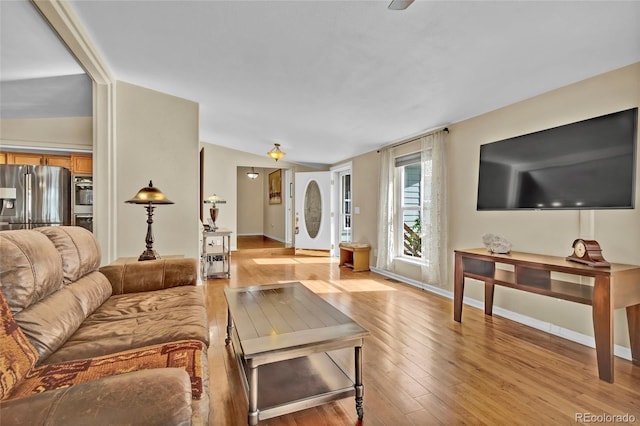 living area featuring baseboards, vaulted ceiling, and light wood finished floors