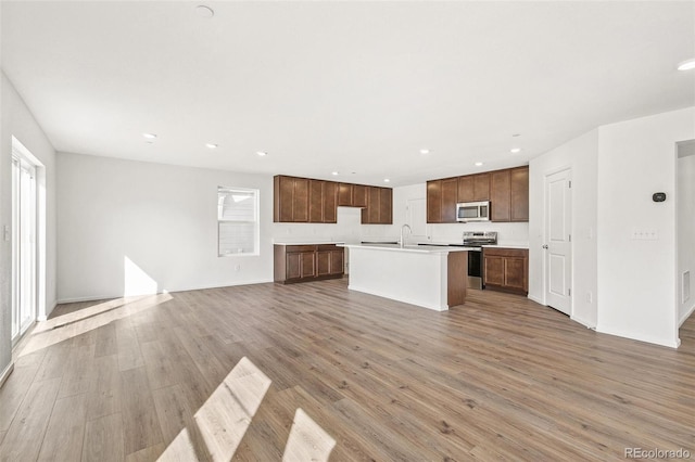 kitchen featuring light wood-style floors, open floor plan, light countertops, appliances with stainless steel finishes, and a center island with sink