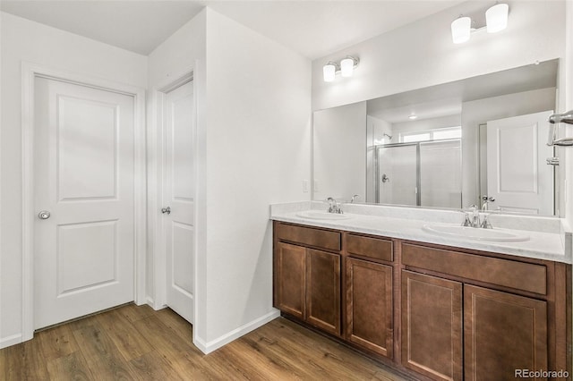 full bath featuring double vanity, wood finished floors, a stall shower, and a sink