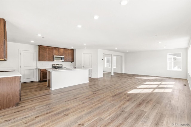 kitchen featuring an island with sink, light wood-style flooring, open floor plan, stainless steel appliances, and light countertops