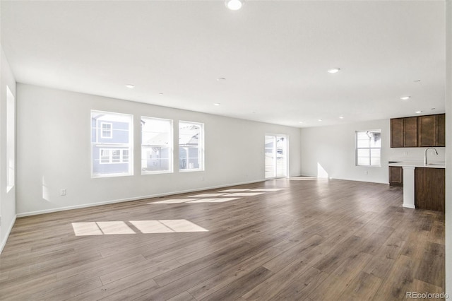 unfurnished living room with recessed lighting, a sink, baseboards, and wood finished floors