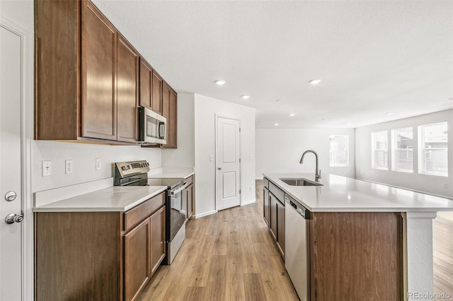 kitchen featuring an island with sink, stainless steel appliances, light countertops, light wood-type flooring, and a sink