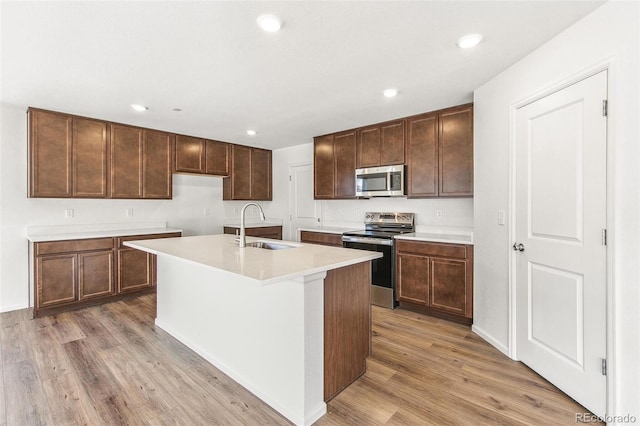 kitchen featuring a sink, light wood-style floors, light countertops, appliances with stainless steel finishes, and a center island with sink