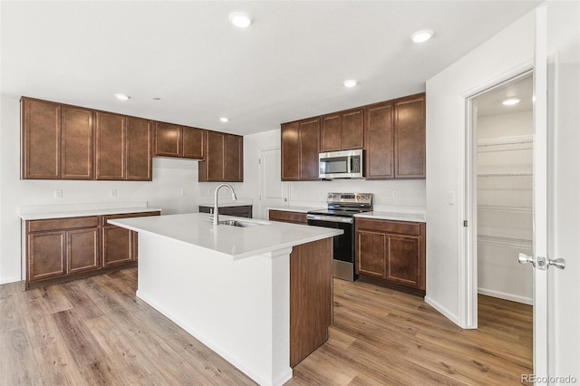 kitchen featuring stainless steel appliances, light countertops, a kitchen island with sink, a sink, and light wood-type flooring