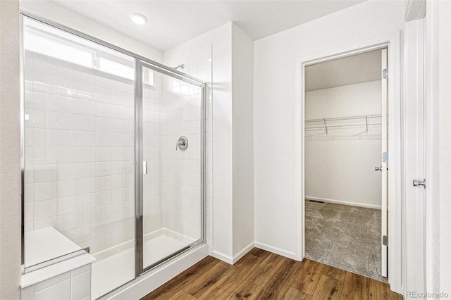 bathroom with a stall shower, baseboards, a walk in closet, and wood finished floors