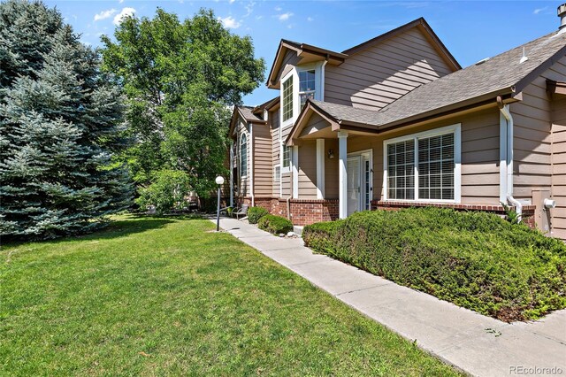 view of front of home featuring roof with shingles, brick siding, and a front lawn