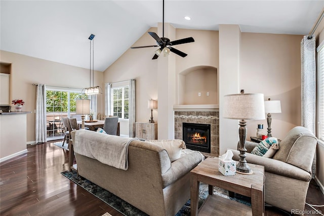 living area featuring dark wood finished floors, a ceiling fan, high vaulted ceiling, a tile fireplace, and baseboards