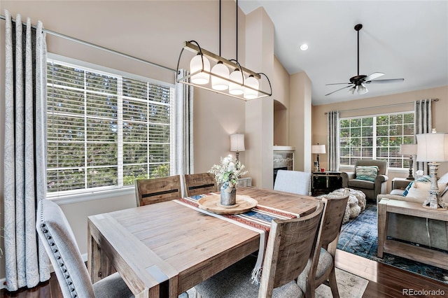 dining area featuring lofted ceiling, recessed lighting, ceiling fan with notable chandelier, a fireplace, and dark wood finished floors