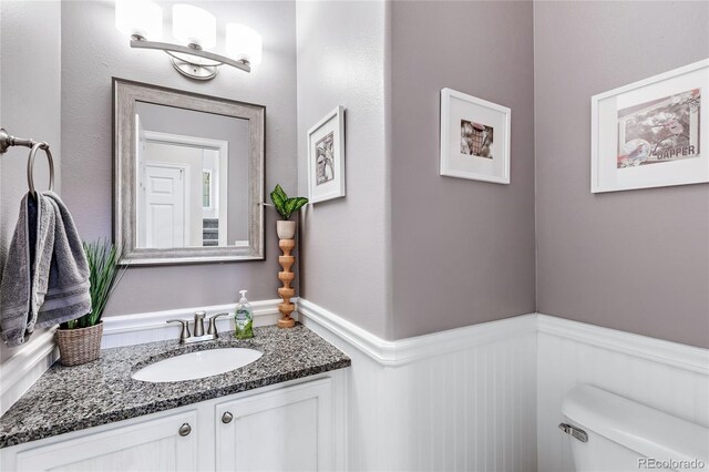 bathroom with toilet, vanity, and wainscoting