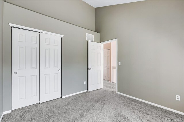 unfurnished bedroom featuring a towering ceiling, visible vents, baseboards, a closet, and carpet