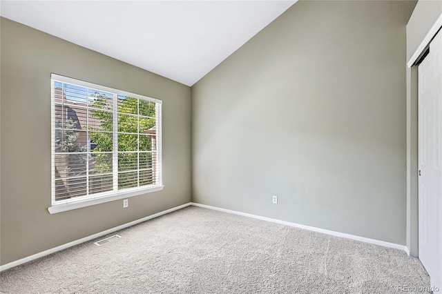 empty room with carpet, visible vents, vaulted ceiling, and baseboards