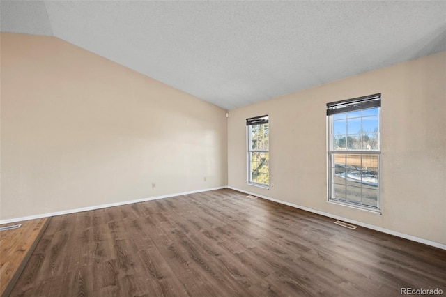 spare room with dark wood-type flooring, a textured ceiling, and vaulted ceiling