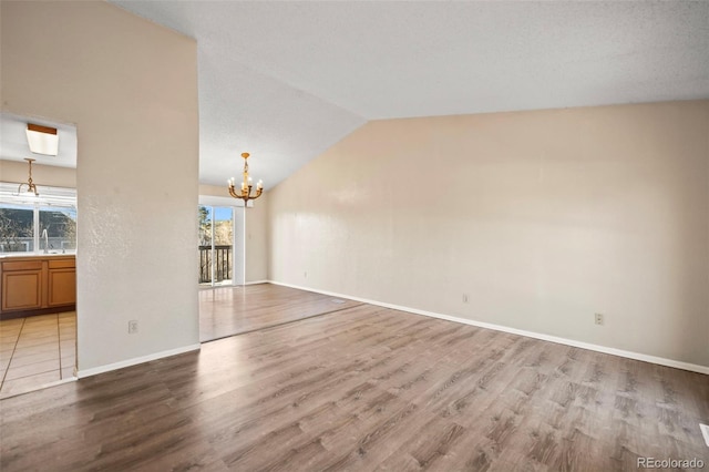 unfurnished living room with light wood-type flooring, lofted ceiling, a notable chandelier, and sink