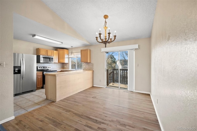 kitchen with lofted ceiling, light hardwood / wood-style floors, kitchen peninsula, hanging light fixtures, and appliances with stainless steel finishes