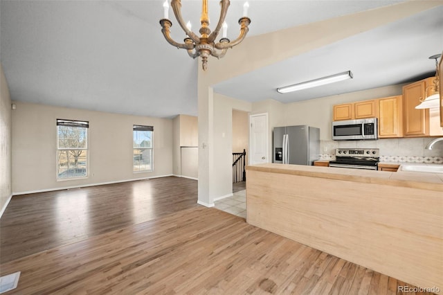 kitchen with an inviting chandelier, stainless steel appliances, light brown cabinets, tasteful backsplash, and decorative light fixtures