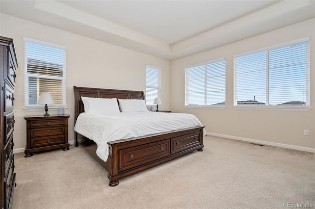 bedroom with a tray ceiling, light carpet, baseboards, and visible vents