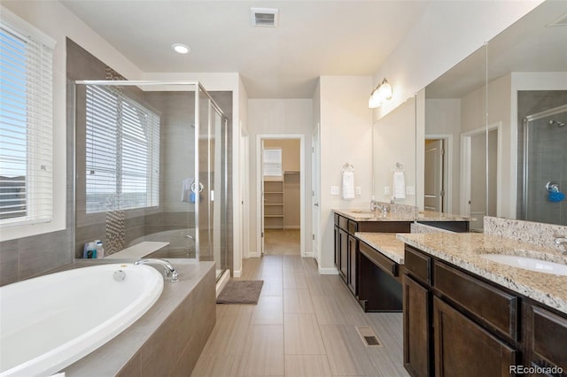 bathroom featuring a walk in closet, a bath, visible vents, a shower stall, and vanity