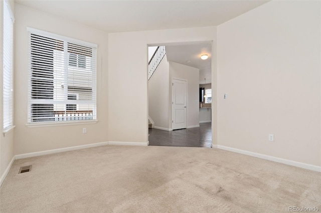 carpeted spare room with baseboards, a wealth of natural light, stairway, and visible vents