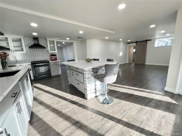 kitchen with a barn door, wall chimney exhaust hood, a kitchen island, black range with electric stovetop, and white cabinets