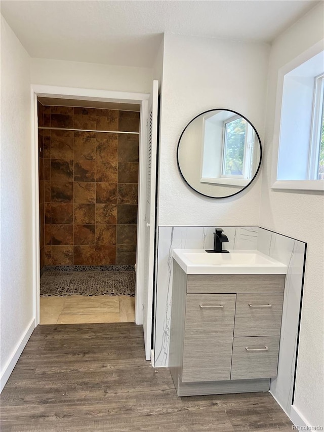 bathroom featuring hardwood / wood-style flooring, a tile shower, and vanity