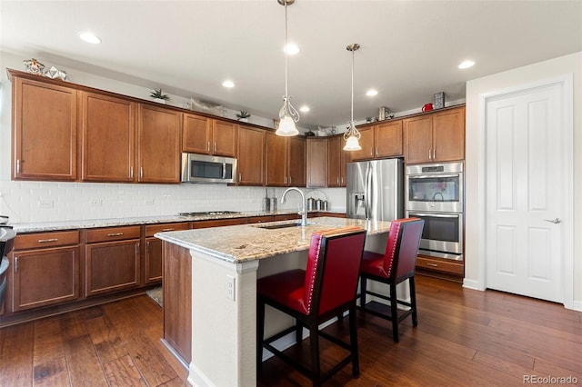 5615 Clover Ridge Cir, Castle Rock, CO 80104 - kitchen featuring appliances with stainless steel finishes, dark wood finished floors, light stone counters, an island with sink, and recessed lighting