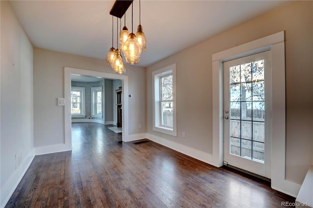 unfurnished dining area featuring a chandelier, dark wood-type flooring, and a healthy amount of sunlight