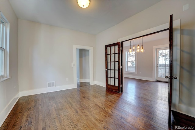 empty room featuring a chandelier, dark hardwood / wood-style flooring, and french doors