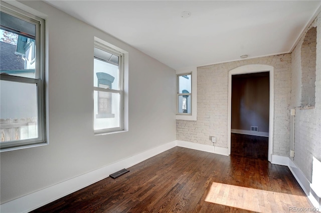 empty room with dark hardwood / wood-style flooring, plenty of natural light, and brick wall