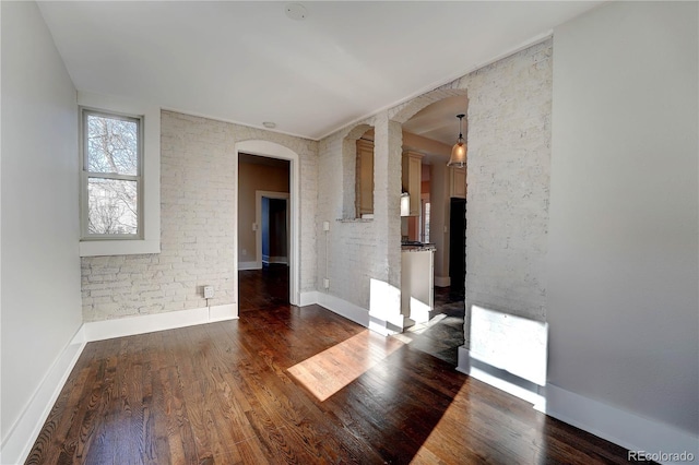 spare room featuring ornate columns, dark hardwood / wood-style flooring, and brick wall