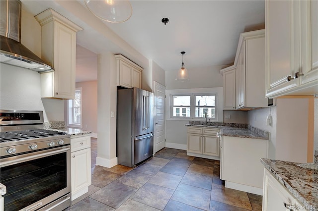 kitchen featuring light stone countertops, sink, hanging light fixtures, stainless steel appliances, and wall chimney range hood